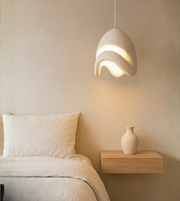 Beige organic wave pendant light hanging over bedside table with minimal décor