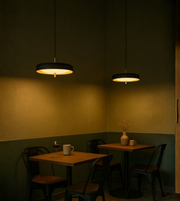 Perforated metal café pendant lights glowing warmly above small tables in a cozy dark-toned dining interior