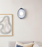 Teardrop-shaped wall sconce with glowing central orb in a modern minimalist interior