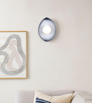 Teardrop-shaped wall sconce with glowing central orb in a modern minimalist interior