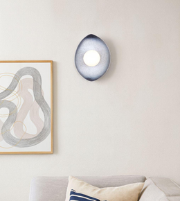 Teardrop-shaped wall sconce with glowing central orb in a modern minimalist interior