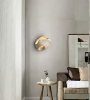 Modern wall sconce on a gray wall with a chair and small table in the foreground.