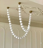 White beaded chandelier hanging from a ceiling with decorative molding.
