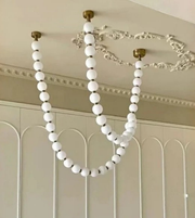 White beaded chandelier hanging from a ceiling with decorative molding.