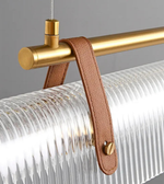 Glass pendant light fixture with gold rod and brown leather strap on a gray background