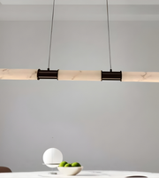 Modern pendant light fixture hanging above a table with a bowl of apples against a gray wall.