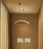 Gold pendant light hanging in a room with beige walls and curtains.