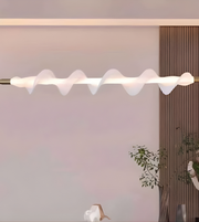 Modern ceiling light fixture with wavy design in a room with a plant and wooden panel.
