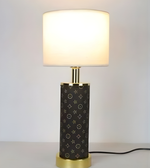 Decorative table lamp with patterned base and white shade on a plain background