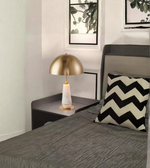 Bedroom corner with a gold lamp on a nightstand and a chevron-patterned pillow.