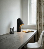 Desk with lamp, book, and chair in a room with a window and curtain.