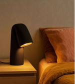 Black table lamp on a wooden nightstand next to a bed with pink pillows.