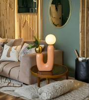Living room with a beige sofa, decorative pillows, a round wooden table with a pink lamp, and a green wall.