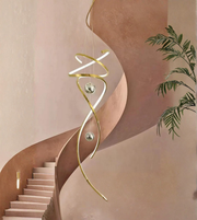 Modern gold spiral pendant light in a stylish interior setting with a staircase and plant.