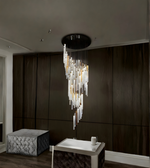 Modern chandelier hanging in a room with dark walls and a textured ottoman.