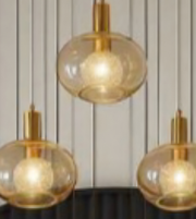 Three gold pendant lights with glass shades on a neutral background