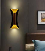 Modern wall sconce on a dark wall with a bed and abstract art in the background