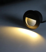 Black outdoor light fixture emitting a warm glow on a dark background