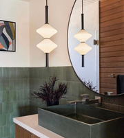 Bathroom interior with green tiles, a round mirror, and pendant lights.