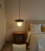 Modern pendant light hanging above a bed in a bedroom setting