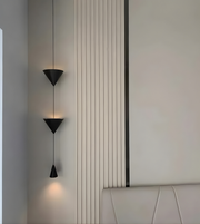 Modern wall-mounted light fixture on a neutral wall with a bed in the background