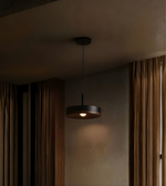 Dark pendant light hanging in a room with curtains and a neutral wall.