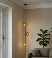 Modern pendant light fixture in a living room setting with a plant and sofa.