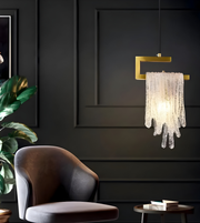 Modern chandelier hanging in a dark room with a chair and plant.
