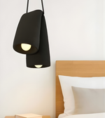 Modern black pendant lamp hanging above a bed with wooden headboard and white pillows.