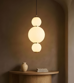 Modern pendant light with three spherical shades hanging above a wooden table with a vase and books.