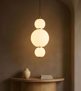 Modern pendant light with three spherical shades hanging above a wooden table with a vase and books.