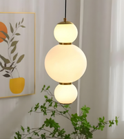 Modern pendant light with three spherical bulbs hanging in a room with a plant and wall art.