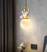 Pendant light with astronaut design on a wall, featuring a moon-shaped bulb.