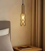 Gold pendant light hanging above a wooden nightstand with a bed in the background