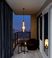 Modern balcony with a chair, small table, and pendant light overlooking a cityscape at night.
