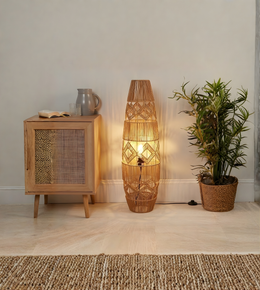 Handwoven boho floor lamp with warm ambient light beside wooden cabinet and indoor plant