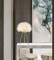 White feather tripod table lamp with gold legs on a console table