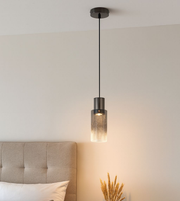 Modern smoked glass cylinder pendant light hanging beside bed creating warm ambient lighting in contemporary bedroom