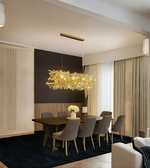 Modern dining room with a gold chandelier, wooden table, and gray chairs.