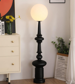 Black floor lamp with a round white light bulb in a room setting.