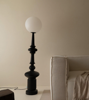 Black floor lamp with a white globe shade next to a beige sofa against a beige wall.