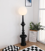 Black floor lamp in a room with a plant and cushions on the floor.