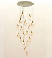 A modern multi-light chandelier pendant fixture with a circular brushed metal ceiling canopy, multiple hanging rods, and twelve clear glass teardrop-shaped bulbs arranged in a cascading diamond pattern against a plain light background.