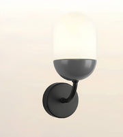 A modern wall-mounted sconce with a matte black circular backplate, curved arm, and bowl-shaped shade, paired with a frosted white dome glass shade, shown against a light beige background.