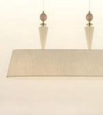 A modern rectangular pendant light with a wide, tapered beige fabric drum shade, two fluted glass cone shades, and round blush pink beads with brass hardware, shown against a plain off-white background.