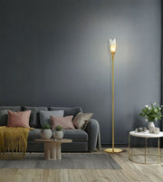 A modern gold floor lamp with a sculptural white leaf-shaped shade stands in a styled living room next to a gray sofa and a small white side table.