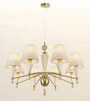 A modern six-light chandelier with a brushed brass/gold metal frame, white fabric drum shades, and clear glass cone accents, suspended from a matching ceiling canopy against a plain off-white background.