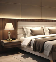 A modern bedroom interior featuring a bed with white linens and taupe pillows, a matching upholstered headboard, a floating wood nightstand with a white table lamp, and warm ambient lighting against a wood-paneled wall.