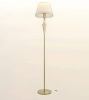 A mid-century modern floor lamp with a tapered white fabric shade, a fluted cream-colored stem, and a slim brass base on a light beige background.