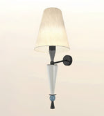 A modern wall sconce light fixture featuring a tapered beige pleated fabric shade, a matte black wall mount and arm, a white glass cone shade, and a small light blue decorative bead accent near the bottom.
